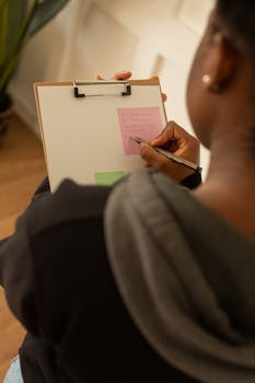 Over-the-shoulder view of a person writing notes on a clipboard indoors.